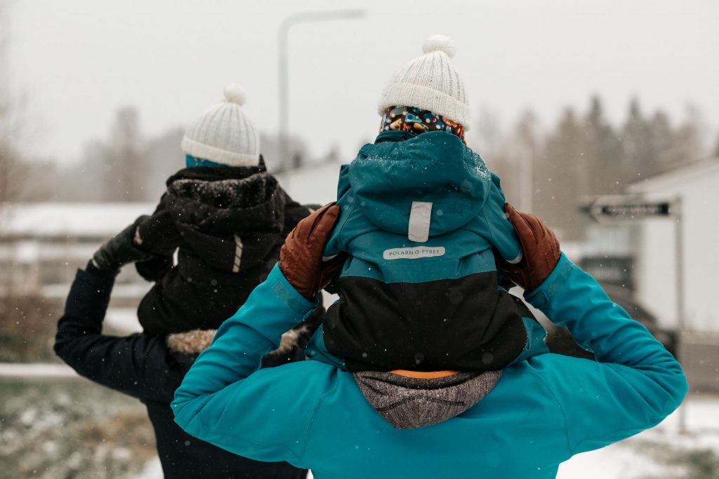 ulkoilua, äiti ja isä kävelevät lapset harteilla talvisessa maisemassa