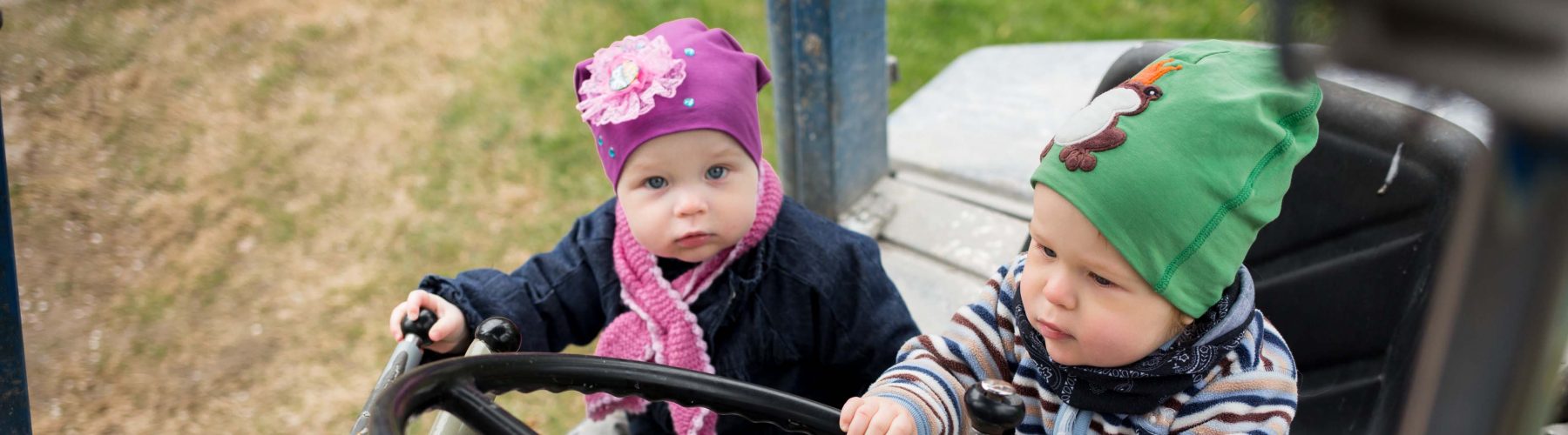1,5v kaksoset, tyttö ja poika ulkona traktorin ratina takana, kevät.