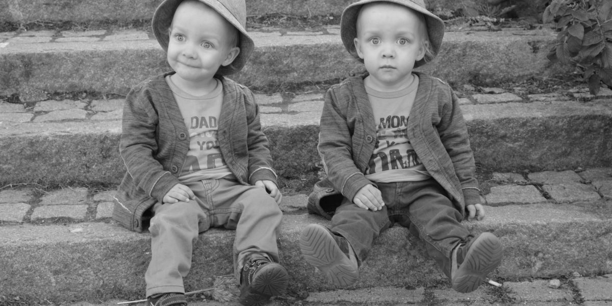 pienet kaksospojat istuvat portailla hatut päässä