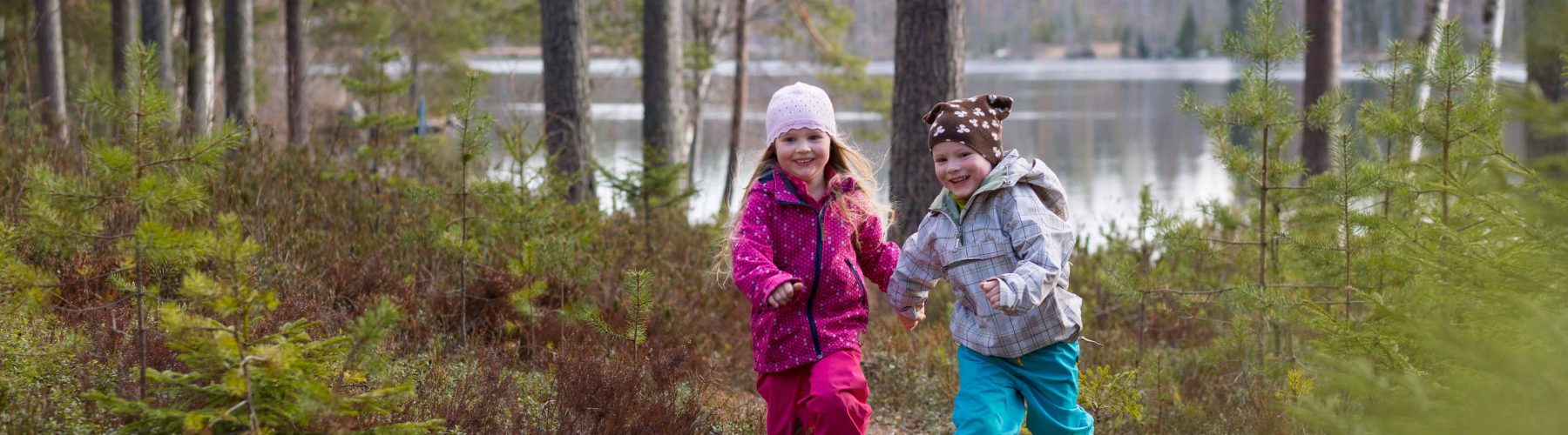 4v kaksoset tyttö ja poika juoksevat metsässä järven rannalla.