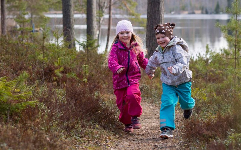 4v kaksoset tyttö ja poika juoksevat metsässä järven rannalla.