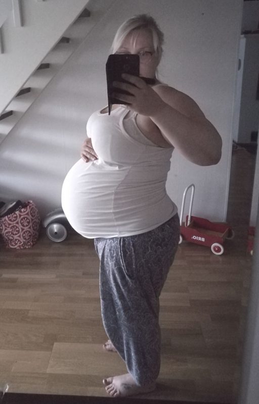 kaksosia odottava nainen peilin edessä ottamassa kuvaa raskausvatsastaan.