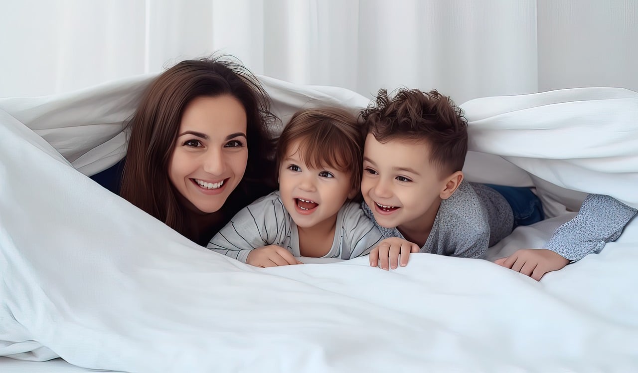 Äiti ja kaksi lasta kurkistavat sängyssä lakanan alta. 