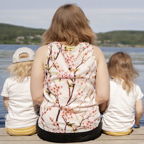 Äiti ja kaksi lasta istuvat laiturilla kasvot järvelle päin.