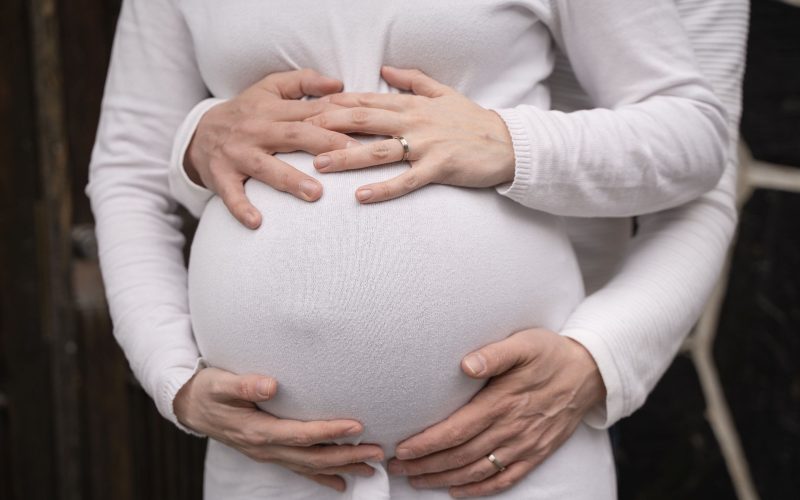 kaksosia odottavan vatsa, jonka ympärillä on kahden vanhemman kädet.