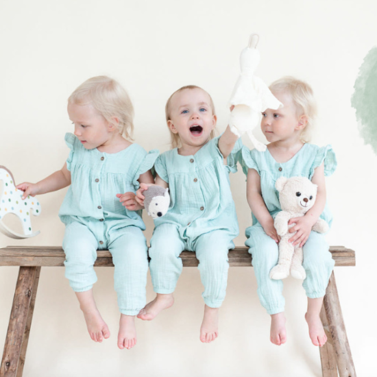 Kolmosten päivä 3.3. Kolme leikki-ikäistä vaaleatukkaista lasta istuu vanhalla puupenkillä rinnakkain pehmolelujen kanssa.