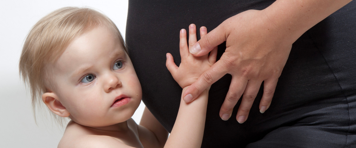 Pieni taapero kuuntelee raskaana olevan vatsan sisään, korva kiinni vatsassa.