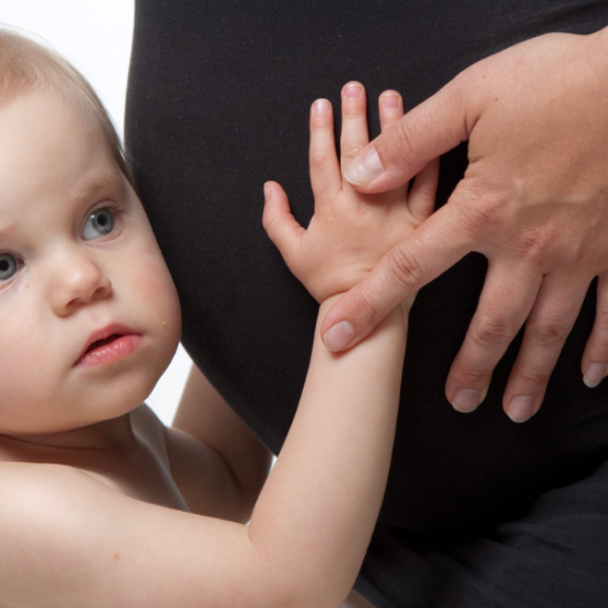 Pieni taapero kuuntelee raskaana olevan vatsan sisään, korva kiinni vatsassa.