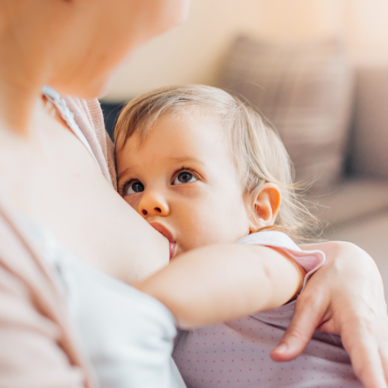 Äiti imettää sylissään taaperoikäistä lasta, joka katsoo äitiä silmiin.