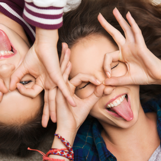 kaksi teini-ikäistä tyttöä näyttää kieltä ja tekee sormillaan silmien ympärille silmälasisangat.