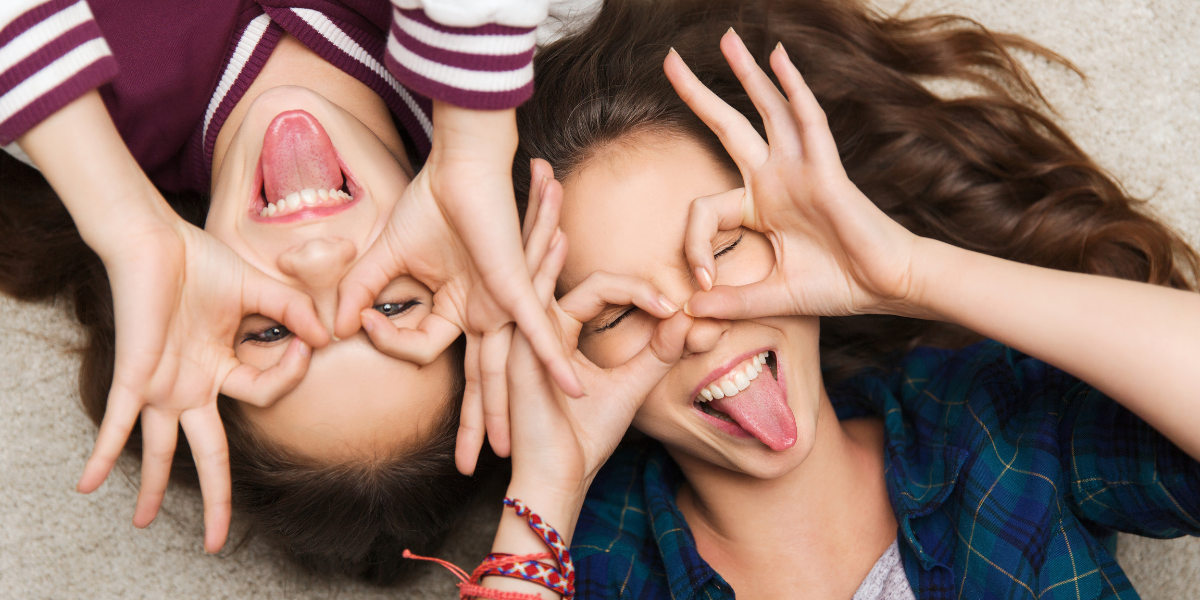 kaksi teini-ikäistä tyttöä näyttää kieltä ja tekee sormillaan silmien ympärille silmälasisangat.