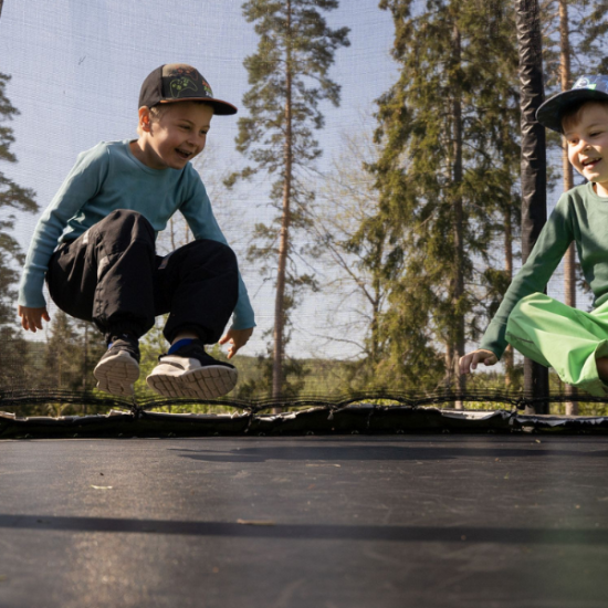 kaksi lasta lippalakit päässä hyppivät trampoliinilla.