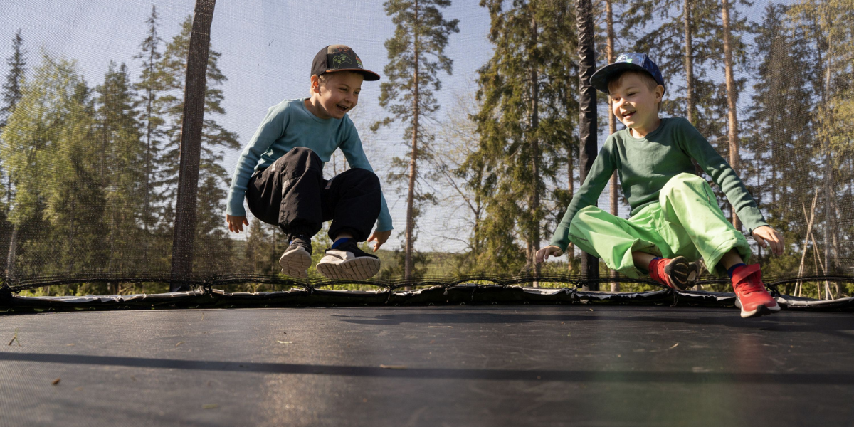 kaksi lasta lippalakit päässä hyppivät trampoliinilla.