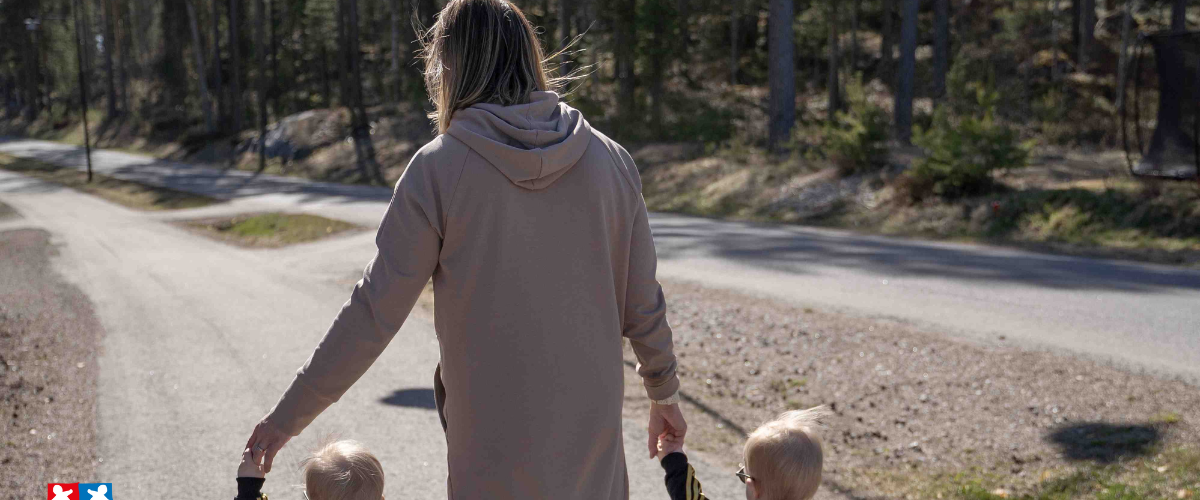 Äiti ja pienet kaksospojat kävelytiellä kävellen käsi kädessä keväisessä säässä.