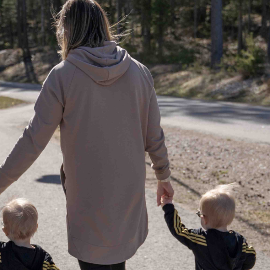 Äiti ja pienet kaksospojat kävelytiellä kävellen käsi kädessä keväisessä säässä.