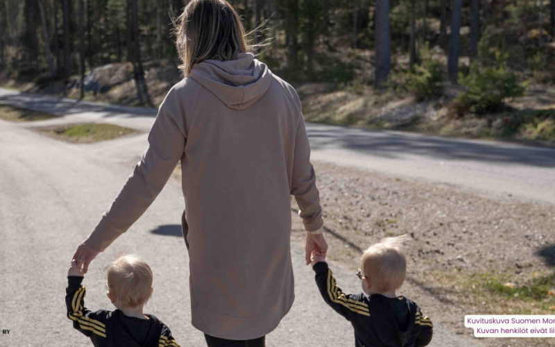 Äiti ja pienet kaksospojat kävelytiellä kävellen käsi kädessä keväisessä säässä.