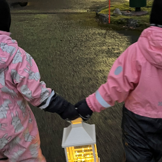 kaksi lasta kantavat yhdessä valolyhtyä kerrostalon pihalla.