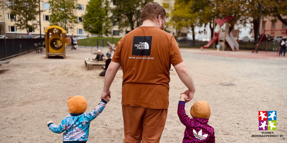 isä kävelee käsi kädessä kahden taaperon kanssa leikkipuistossa.