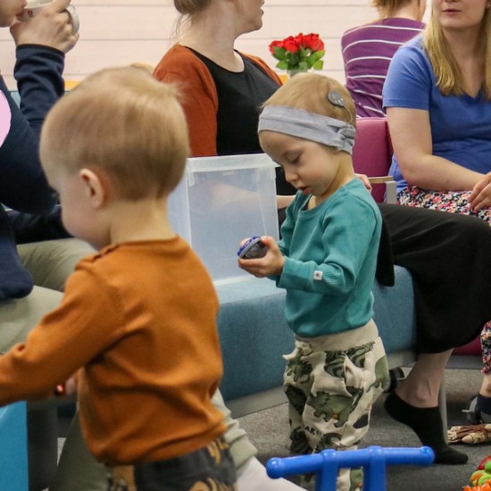 Teksti vastaa kyselyyn. Kolme taaperoikäistä lasta tutkii leluja ja kolme äitiä kuvan taustalla juttelevat.