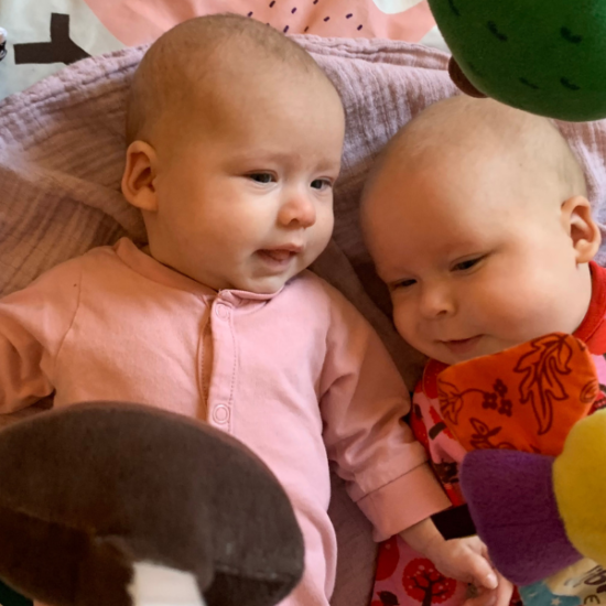 Kaksi vauvaa makoilee leikkikehän alla.