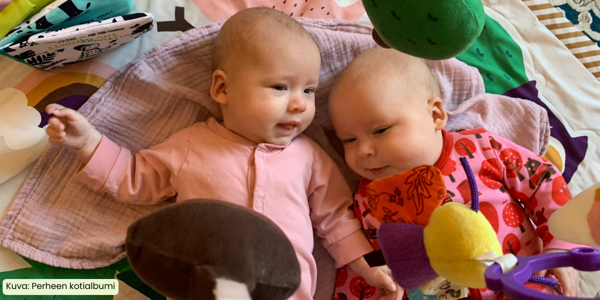 Kaksi vauvaa makoilee leikkikehän alla.